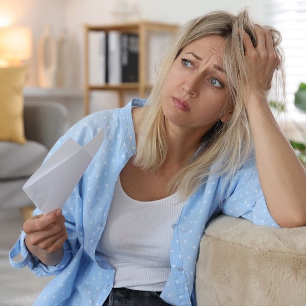 A woman is sitting on a couch, fanning herself with a piece of paper in need of Bioidentical Hormone Replacement Therapy (BHRT)