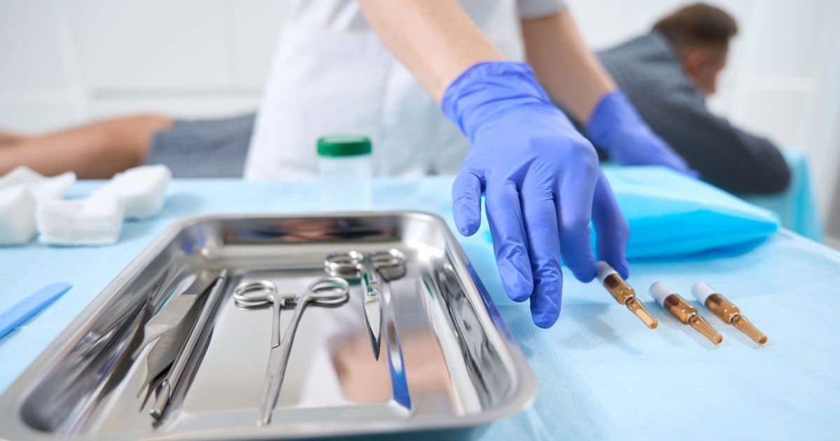 A nurse wearing blue gloves is reaching for a tray of surgical instruments during Bioidentical Hormone Replacement Therapy NYC