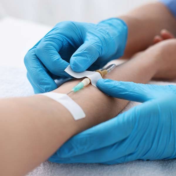 A person in blue gloves is giving a Chelation IV Treatment to a patient