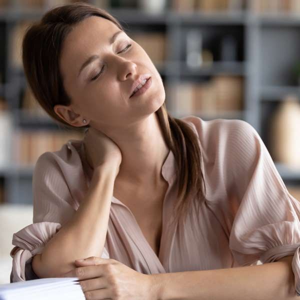 A woman is sitting at a table with her eyes closed representing Chronic Fatigue Syndrome Treatments