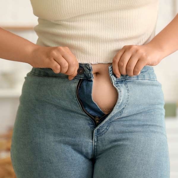Sudden weight gain is a symptom of Cushing's Syndrome A woman is trying to zip up her jeans needing Cushing's Syndrome Treatments