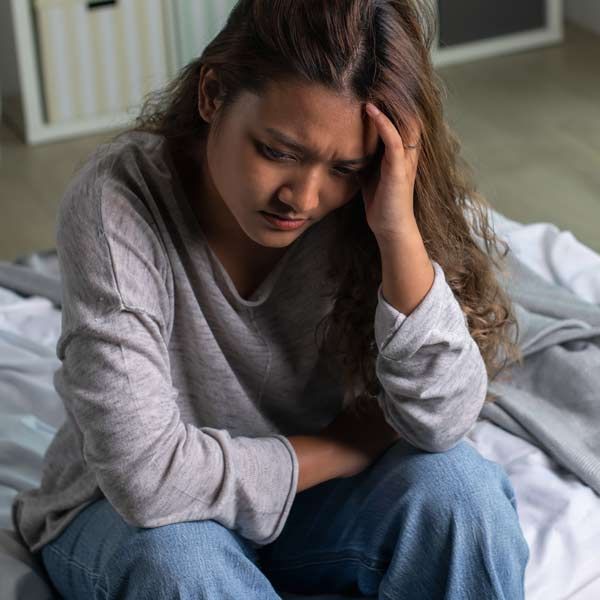 A woman is sitting on a bed with her head in her hands after missing her Depression IV Treatment