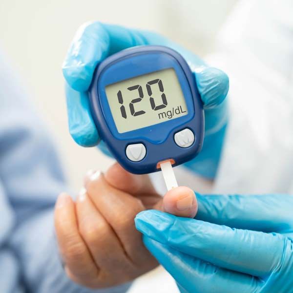 A person wearing blue gloves is holding a device that reads 120 mg/dl, showing her diabetic patient's proper blood sugar levels resulting from Diabetes IV Treatments