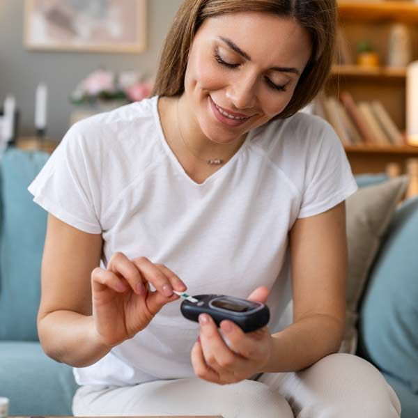 A woman is sitting on a couch using a glucose meter in support of her Diabetes Management Treatments