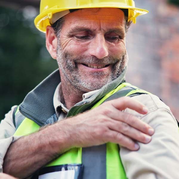Construction worker in a yellow hard hat and reflective vest, looking down in pain needing Personalized Fibromyalgia Medical Therapy by Salerno Wellness in Manhattan, NY, and Connecticut