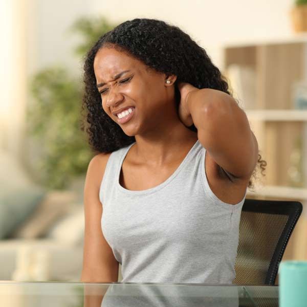 A woman is sitting at a table with her hand on her neck representing Fibromyalgia Treatments