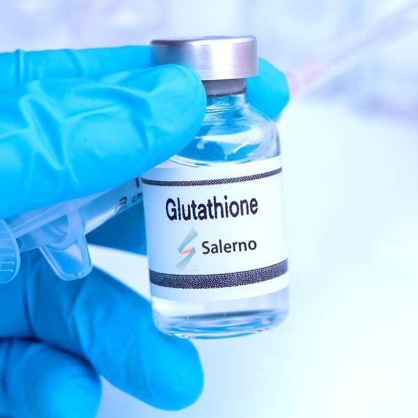 A person wearing blue gloves is holding a bottle of glutathione, representing Glutathione IV Treatments