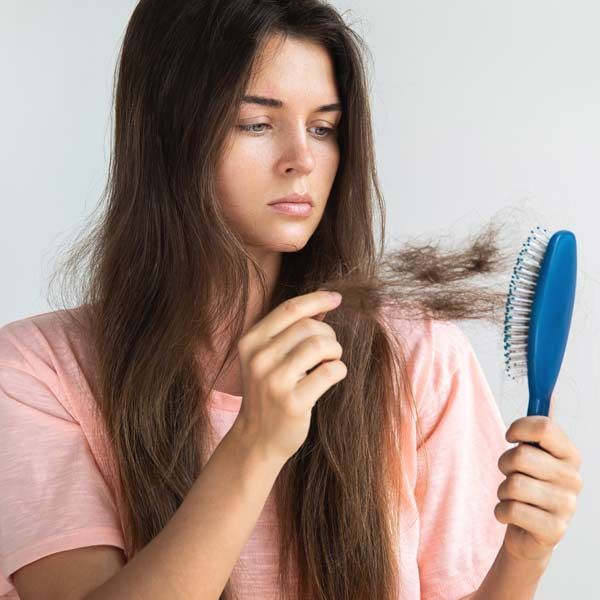 A woman with brown hair looks concerned, holding her hair loss from a blue brush needing Comprehensive and Personalized Hair Loss Therapy by Salerno Wellness in Manhattan, NY, and Connecticut