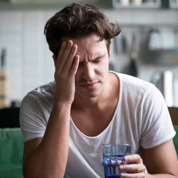 A man sits on a couch, holding a glass of water needing Hangover Helper IV Treatments