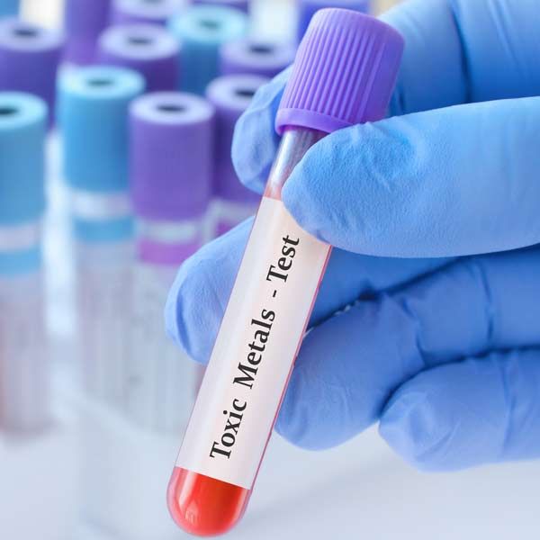 A person wearing blue gloves is holding a test tube that says toxic metals test representing Heavy Metal Detox Treatments