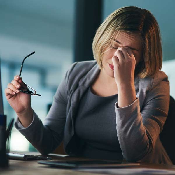 A woman is sitting at a desk holding her glasses and rubbing her eyes, needing Heavy Metal Challenge Testing at Salerno Wellness in Manhattan, NY, and Connecticut