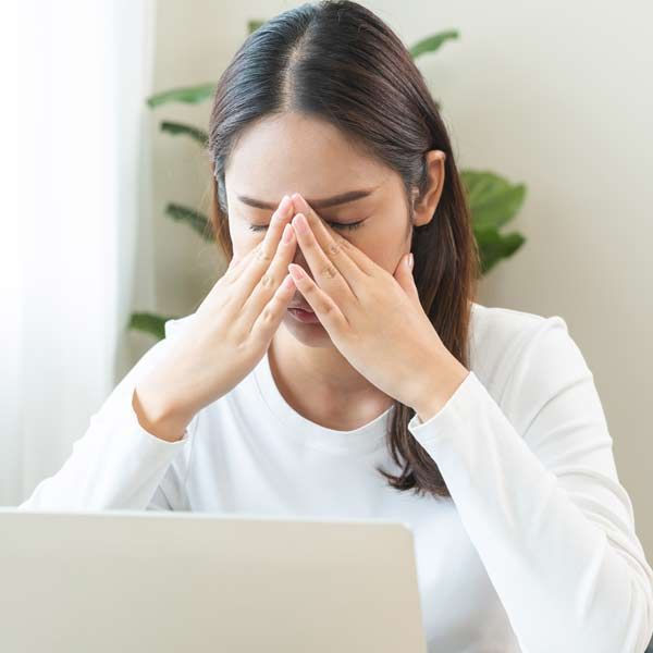 Chronic fatigue is a leading symptom of Hypothyroidism A woman is sitting in front of a laptop computer covering her face with her hands needing Hypothyroidism Treatments