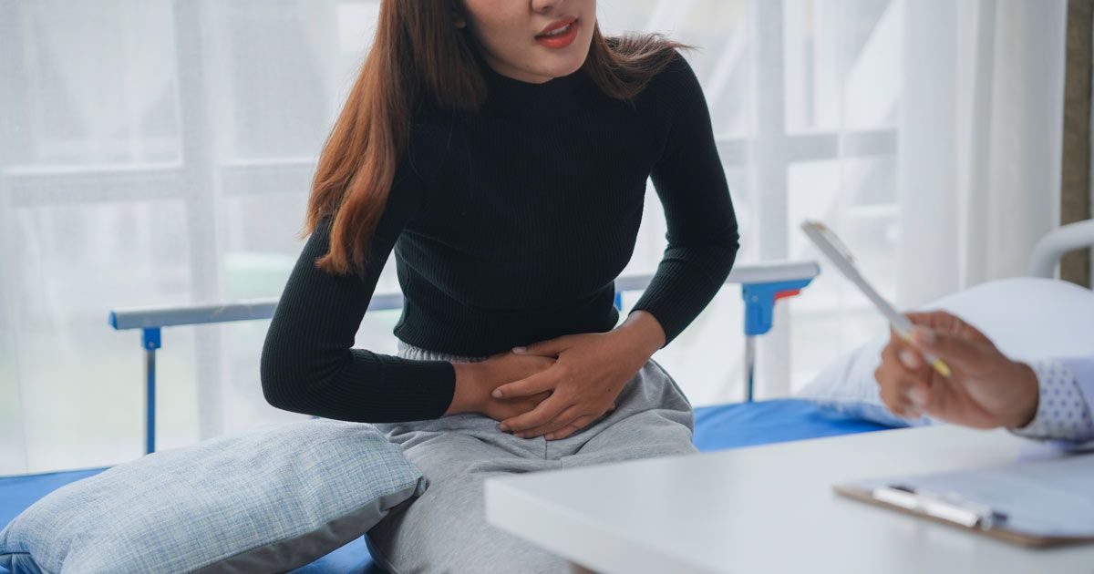 Woman with Irritable Bowel Syndrome consults a doctor in a medical setting. She clutches her abdomen while looking concerned, needing IBS Treatments NYC by Dr. John Salerno