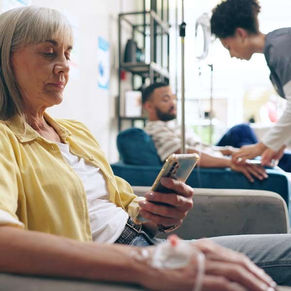 A woman is sitting in a chair, looking at her cell phone while getting IV Treatments for Her