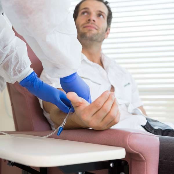 A man is sitting in a chair with a nurse holding his hand. While getting IV Treatments for Him