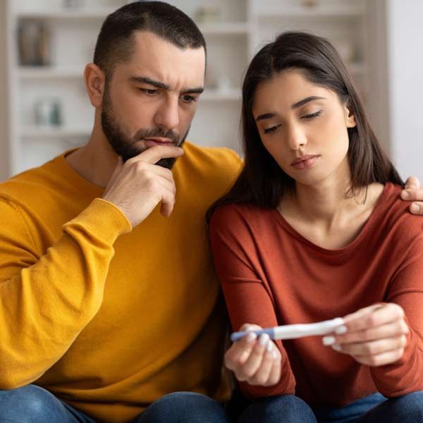 A man and a woman are sitting on a couch looking at a pregnancy test representing Infertility Treatments