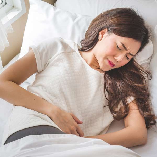 Abdominal cramps and Diarrhea are common symptoms of IBD. A woman is lying in bed with her hands on her stomach, needing Inflammatory Bowel Disease (IBD) Treatments
