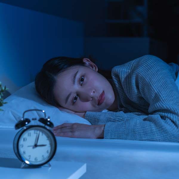 A woman is lying in bed next to an alarm clock representing Insomnia Treatments