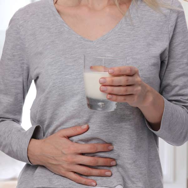 A woman is holding a glass of milk in front of her stomach needing Lactose Intolerance Treatments