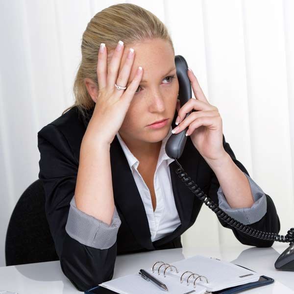 Woman with a Leaky Gut in a suit, looking fatigued and stressed, on the phone. Hand on forehead, notebook on desk needing Functional and Integrative Medical Treatments for Leaky Gut Syndrome at Salerno Wellness in Manhattan, NY, and Connecticut