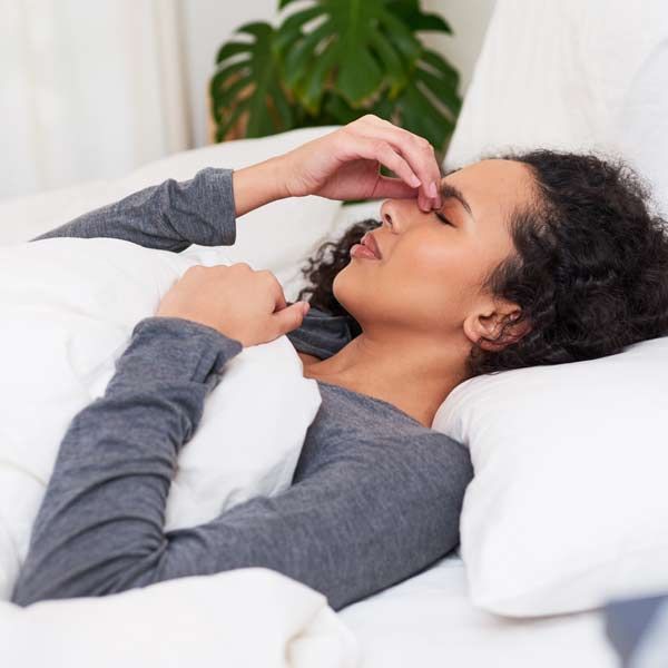 A woman is lying in bed with her hand on her nose, waiting to get her Long COVID IV Treatments