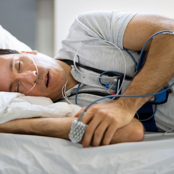 A man is lying in a hospital bed with an oxygen mask on his nose, getting Sleep Apnea Tests