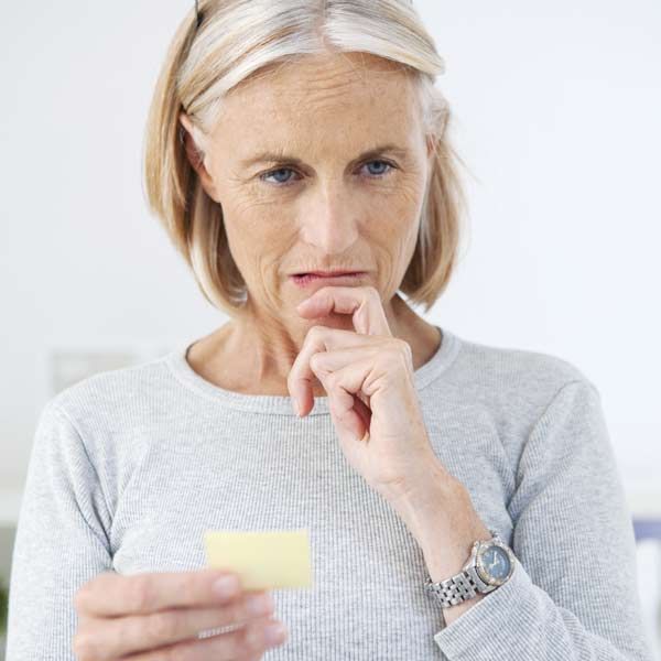 A woman wearing a watch is holding a piece of paper in her hand trying to remember her Memory Function IV Treatments