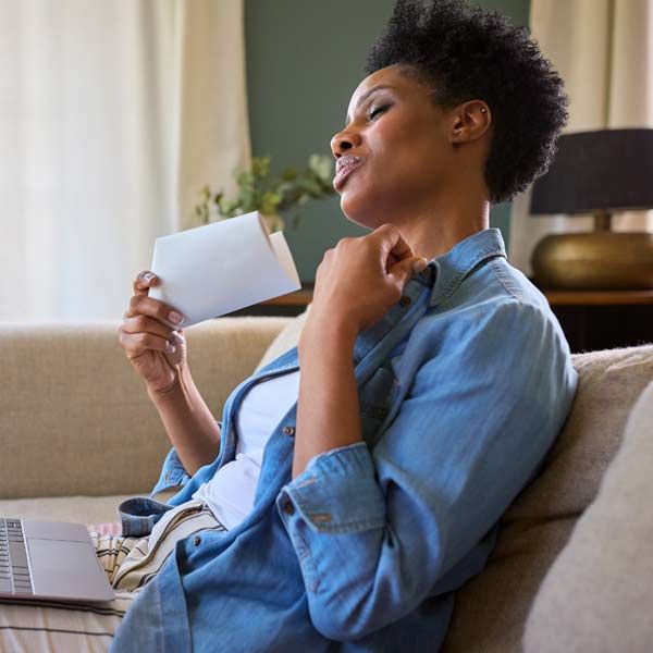 A woman is sitting on a couch holding a piece of paper, considering Natural Treatments that Complement Traditional Medical Care for Severe or Chronic Menopause Symptoms by Salerno Wellness in Manhattan, NYC, and Connecticut