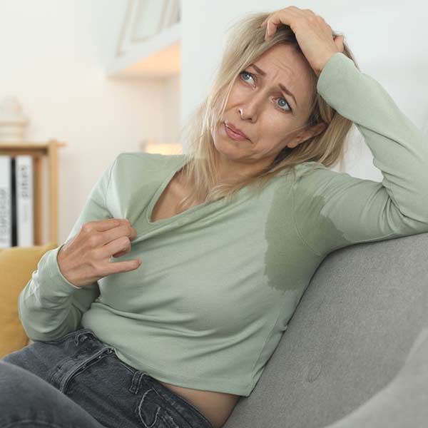 A woman is sweating while sitting on a couch needing Menopause Treatments