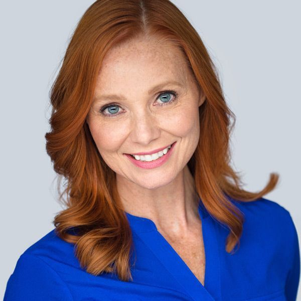 A woman with red hair is wearing a blue shirt and smiling, happy with her Lutronic Genius Skin Rejuvenation