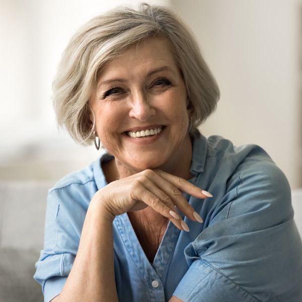 A woman in a blue shirt is smiling with her hand on her chin happy with her TwinLight Fractional Rejuvenation