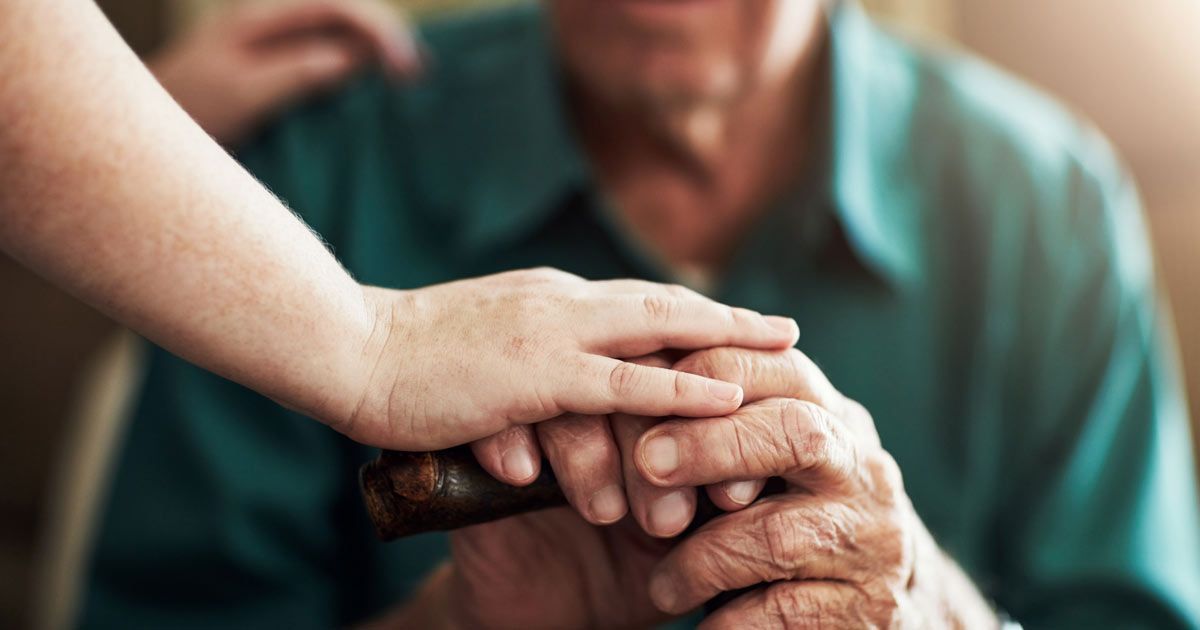 Person's hand holding an elderly person's hand, both resting on a cane. Soft lighting and empathy, Neurodegenerative Disease Treatments NYC - Dr. John Salerno