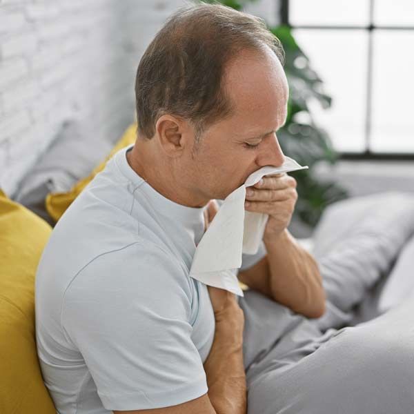 Man in bed blowing his nose with a tissue a candidate for IV Ozone Therapy