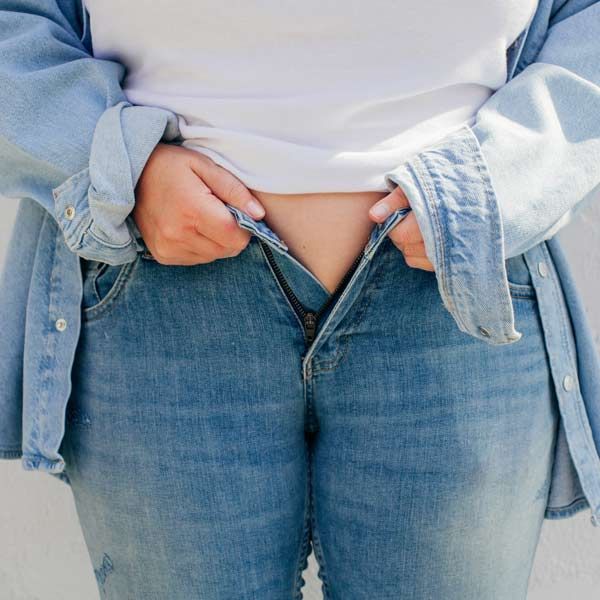 Sudden Weight Gain is a Symptom of PCOS A woman wearing a white shirt and blue jeans that are too tight from sudden weight gain needs Comprehensive Integrative and Functional Medical Treatments for PCOS at Salerno Wellness in Manhattan, NYC, and Connecticut