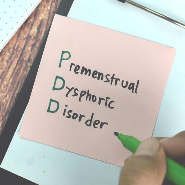 A person is writing on a piece of paper that says Premenstrual Dysphoric Disorder - PMDD