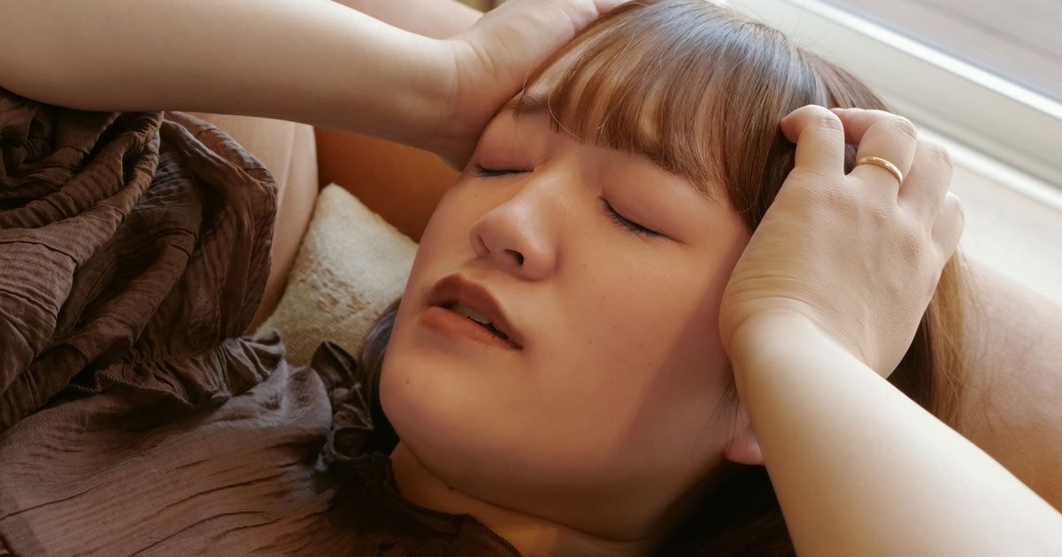 A woman is lying on a bed with her eyes closed and her hands on her head before going to her PMDD Treatments NYC with Dr. John Salerno