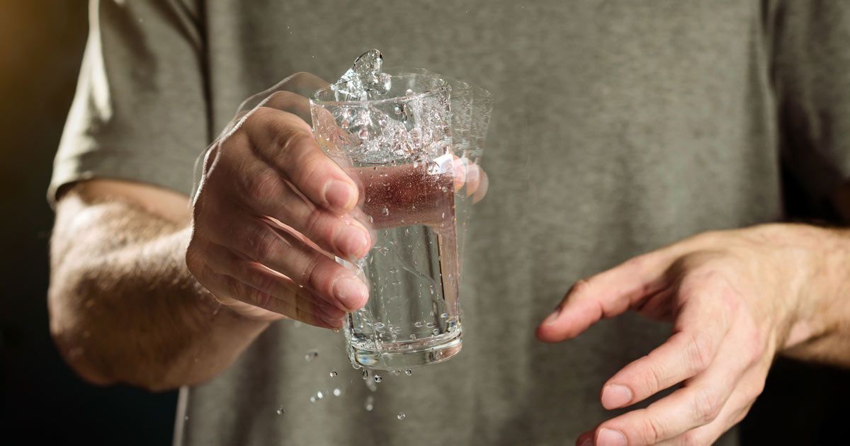 A person's hand shaking a glass of water mid-air, droplets and fragments visible showing a need for Parkinson's Disease Treatments NYC by Dr. John Salerno