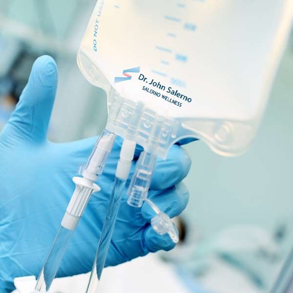 A hand in a blue glove is holding a bag that says dr. john salerno Personalized IV Treatments