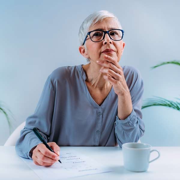 An older woman is sitting at a table, writing on a piece of paper representing Phosphatidylcholine IV Treatments