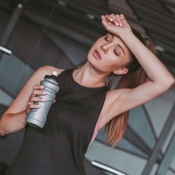 A woman is holding a water bottle and wiping her forehead after her Recovery Plus IV Treatments