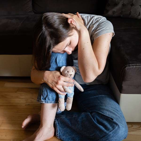 A woman is sitting on the floor holding a teddy bear representing Recurrent Pregnancy Loss Treatments