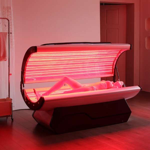 A woman is laying on a tanning bed with red lights on it getting Red Light Therapy