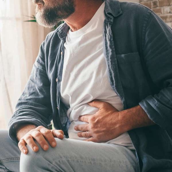 Diarrhea, abdominal pain and cramping are the most common symptoms of Short Bowel Syndrome A man is sitting on a couch holding his stomach in pain indicating Short Bowel Syndrome Treatments