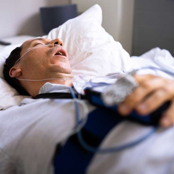 A man is lying in bed with an oxygen mask around his neck, indicating a need for Complementary Medical Sleep Apnea Treatments at Salerno Wellness in Manhattan, NY, and Connecticut