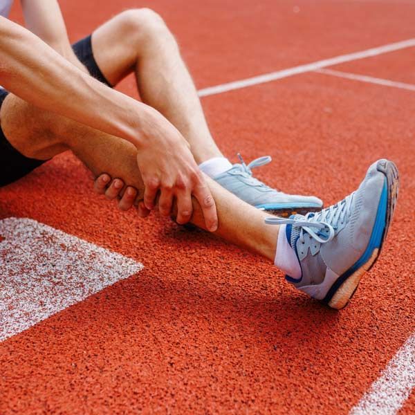 A person is lying on the ground on a track holding their ankle representing Sports Injury Treatments