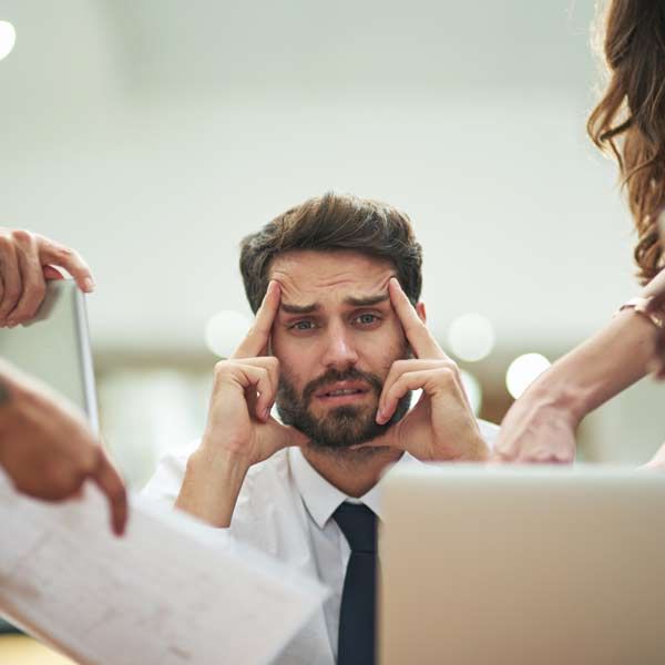 A man with a beard is sitting in front of a laptop computer with his hands on his head Representing Stress Management Treatments