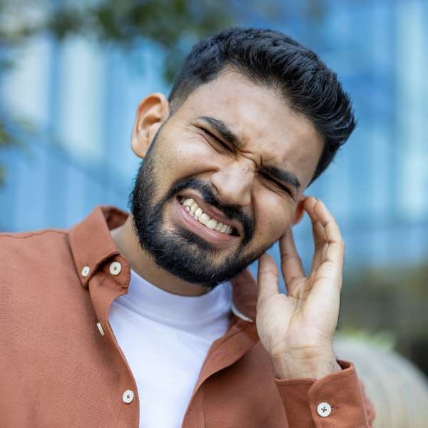 Man with a beard and closed eyes, touching his ear, a candidate for Tinnitus Treatment by Dr. John Salerno