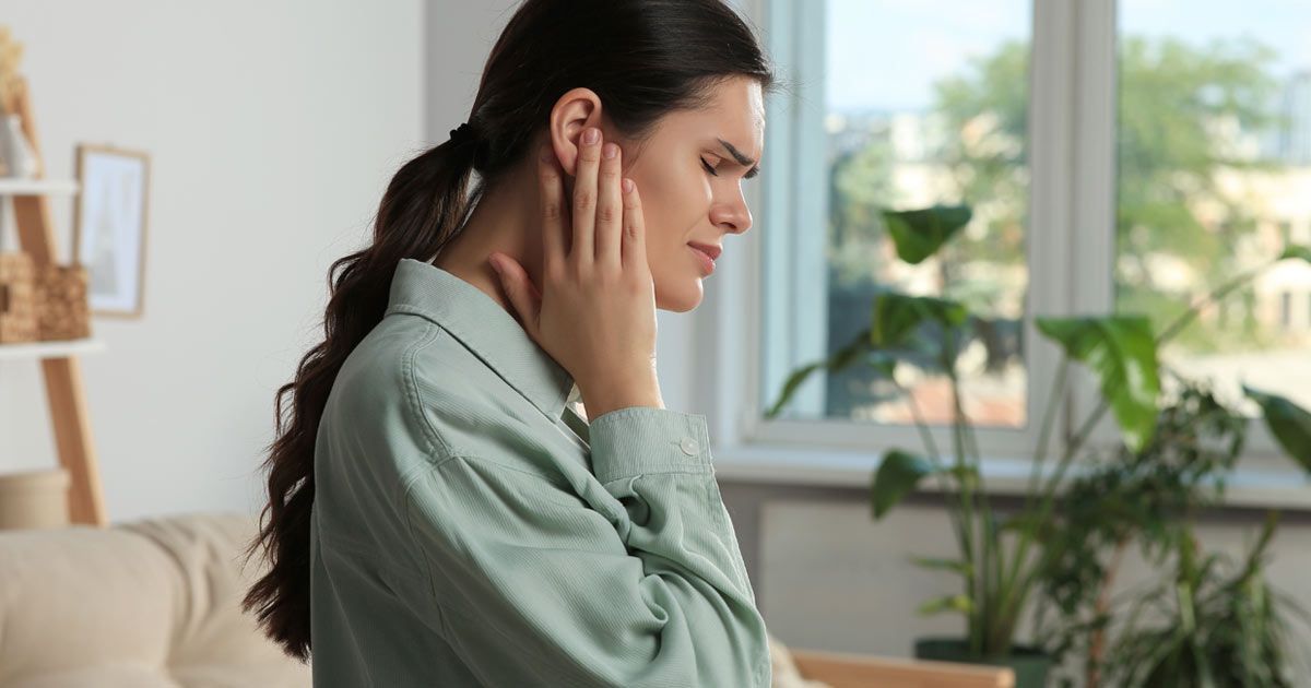 Woman in light green shirt touching her ear, needing Tinnitus Treatments NYC by Dr. John Salerno