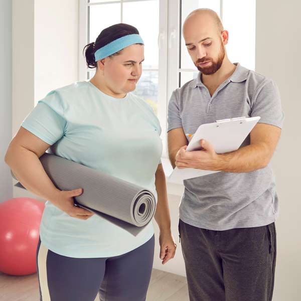 A man is holding a clipboard, and a woman is holding a yoga mat starting Exercise Programs for Weight Loss