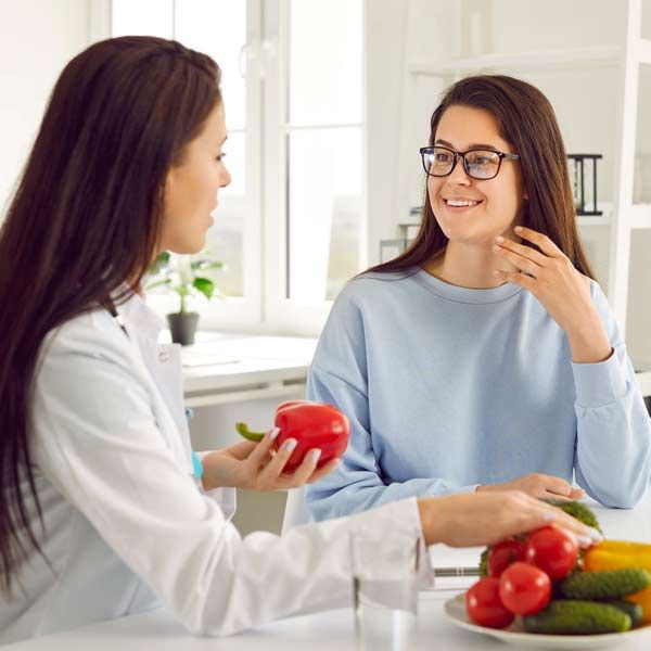 Two women are sitting at a table with a plate of fruit and vegetables, discussing Nutritional Counseling for Weight Loss